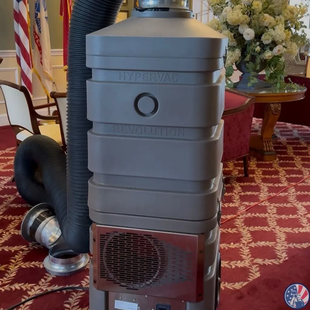 HyperVac Hybrid duct cleaning vacuum inside an elegant room with flags and flowers in the background.