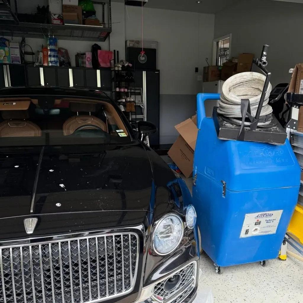 Professional duct cleaning equipment beside a luxury car in a garage—highlighting the benefits of duct cleaning in Alexandria VA.