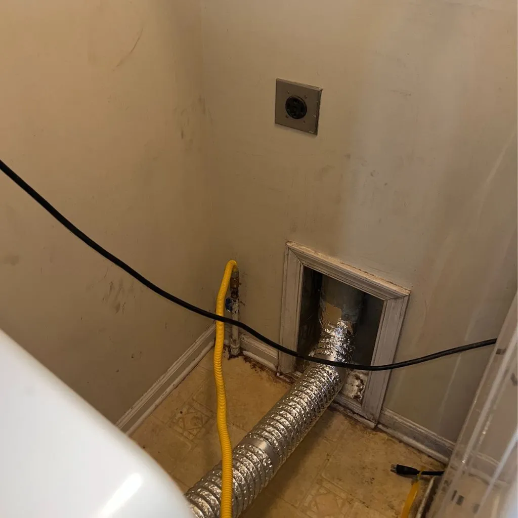 Clogged Dryer Vent Fire Risk in Alexandria VA showing lint buildup inside wall vent behind dryer before professional cleaning