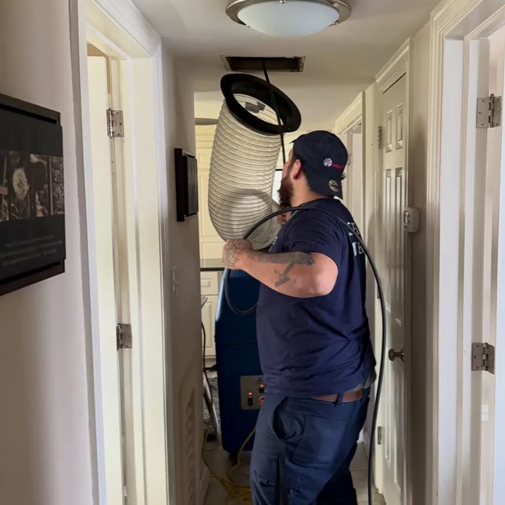 Technician attaching a heavy-duty vacuum hose to a ceiling vent to remove the debris causing clogged ducts and sinus problems.