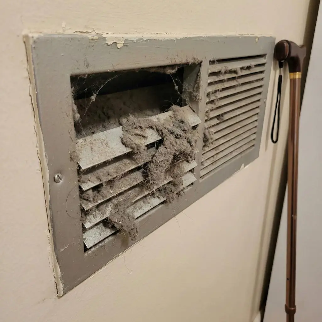 Heavily clogged wall vent next to a walking cane, illustrating the respiratory hazards associated with seniors and dirty air ducts.
