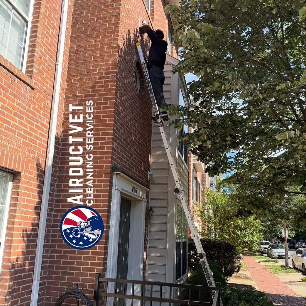 AirDuctVet technician on extension ladder providing Raleigh Durham Triangle duct cleaning service for a brick townhome exterior vent