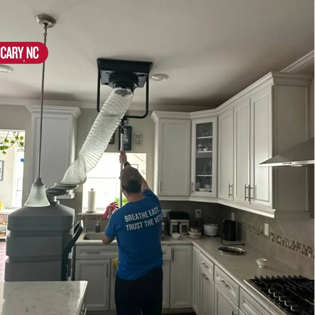 AirDuctVet technician cleaning a kitchen ceiling vent with hose equipment during an air duct cleaning Cary NC service call